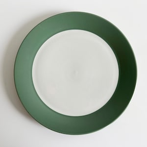 May include: A green and white ceramic dinner plate. The plate has a wide green rim and a white center.