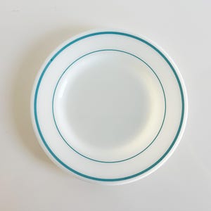 May include: A white ceramic plate with a teal blue rim and a single teal blue line around the center.