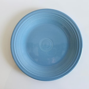 May include: A round, light blue ceramic plate with concentric rings near the rim and a central circular design. The plate has a glossy finish and is set against a white background. This is a classic dinnerware item.