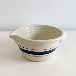 May include: A white ceramic mixing bowl with a blue stripe around the rim. The bowl has a pouring spout and a handle.
