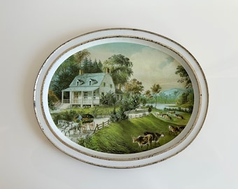 May include: A white oval metal tray with a raised rim and a painted scene of a white farmhouse with a green lawn, trees, and a river in the background. There are cows and a horse-drawn wagon in the scene.