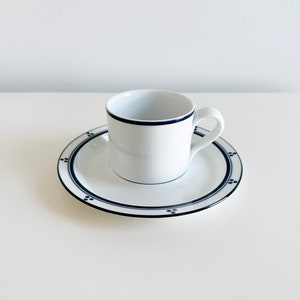 May include: A white porcelain coffee cup with a blue rim and a matching saucer with a blue rim and a blue dot pattern.