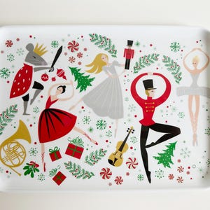 May include: White ceramic serving tray with a festive Christmas Nutcracker theme. The tray features a Nutcracker, a ballerina, a mouse, and a Christmas tree. The tray is decorated with red, green, and gold accents.