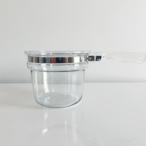 May include: A clear glass double boiler with a silver metal rim and a clear plastic handle.