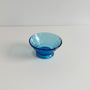 May include: A small, blue glass bowl with a textured, dimpled surface. The bowl has a flared rim and a small, round base.