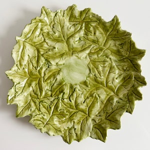 May include: A green ceramic serving dish shaped like a large leaf with a raised design. The dish is perfect for serving snacks, appetizers, or desserts.