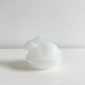 May include: A white ceramic bunny shaped butter dish with a lid. The bunny is sitting in a nest.
