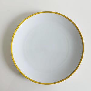 May include: A white ceramic plate with a bright yellow border. The plate is round and has a simple, elegant design. The yellow border adds a pop of color to the otherwise plain white surface. This plate is suitable for serving food.