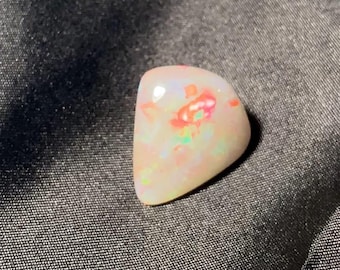 May include: A polished, pearly white opal gemstone with vibrant flashes of red, orange, and green. The stone has a smooth, rounded shape and a glossy surface, showcasing its natural beauty. This gemstone is ideal for jewelry making.