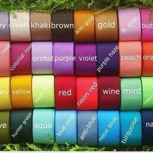 May include: A collection of colorful ribbon spools in various shades, including black, white, grey, and vibrant hues like hot pink, neon orange, and navy royal. Each spool is labeled with its color name.