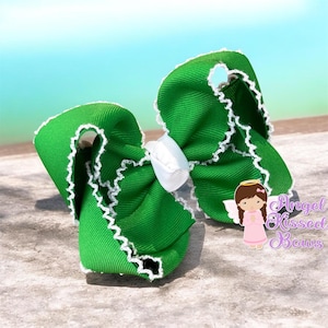 May include: A bright green hair bow made of ribbed fabric with a white scalloped edge trim. The center of the bow is cinched with a small white ribbon knot. A small graphic of an angel with the text Angel Kissed Bows is visible on the right.