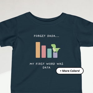 May include: A dark blue baby t-shirt with a graphic of a dinosaur standing on a bar graph. The text on the shirt reads "Forget Dada... My first word was DATA + More Colors!"