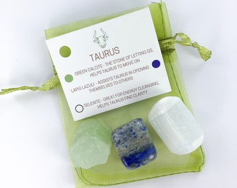 May include: A green pouch with a white card that says "Taurus" and lists three crystals: green calcite, lapis lazuli, and selenite. The card describes the properties of each crystal for the Taurus zodiac sign.