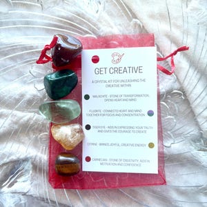 May include: A red organza bag containing a set of six crystals: malachite, fluorite, tiger eye, citrine, and carnelian. A white card inside the bag reads "Get Creative" and describes the properties of each crystal.