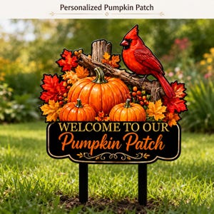 May include: A decorative yard sign featuring a bright red cardinal perched on a wooden branch above three orange pumpkins and colorful autumn leaves. The black sign displays the text "WELCOME TO OUR Pumpkin Patch" in gold lettering.