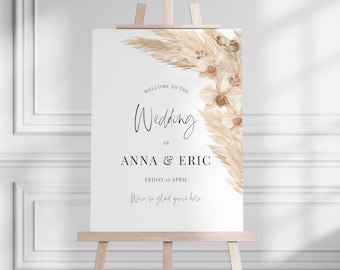 May include: A wedding welcome sign on a wooden easel. The sign features elegant calligraphy announcing the wedding of Anna & Eric on April 12th. Floral accents in beige and cream adorn the top right corner.
