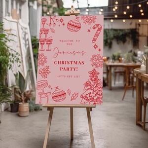 a pink sign with festive Christmas-themed illustrations and text, placed in a room with plants and string lights.