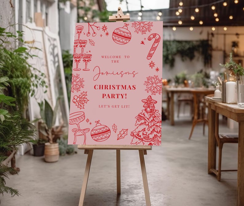 a pink sign with festive Christmas-themed illustrations and text, placed in a room with plants and string lights.