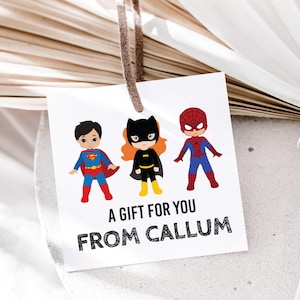 May include: A white gift tag with a black border featuring three cartoon superheroes: Superman, Batgirl, and Spiderman. The tag reads "A gift for you from Callum".