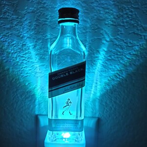 May include: A clear glass bottle night light shaped like a Johnnie Walker Double Black whisky bottle. The bottle is lit from the inside with a blue light.