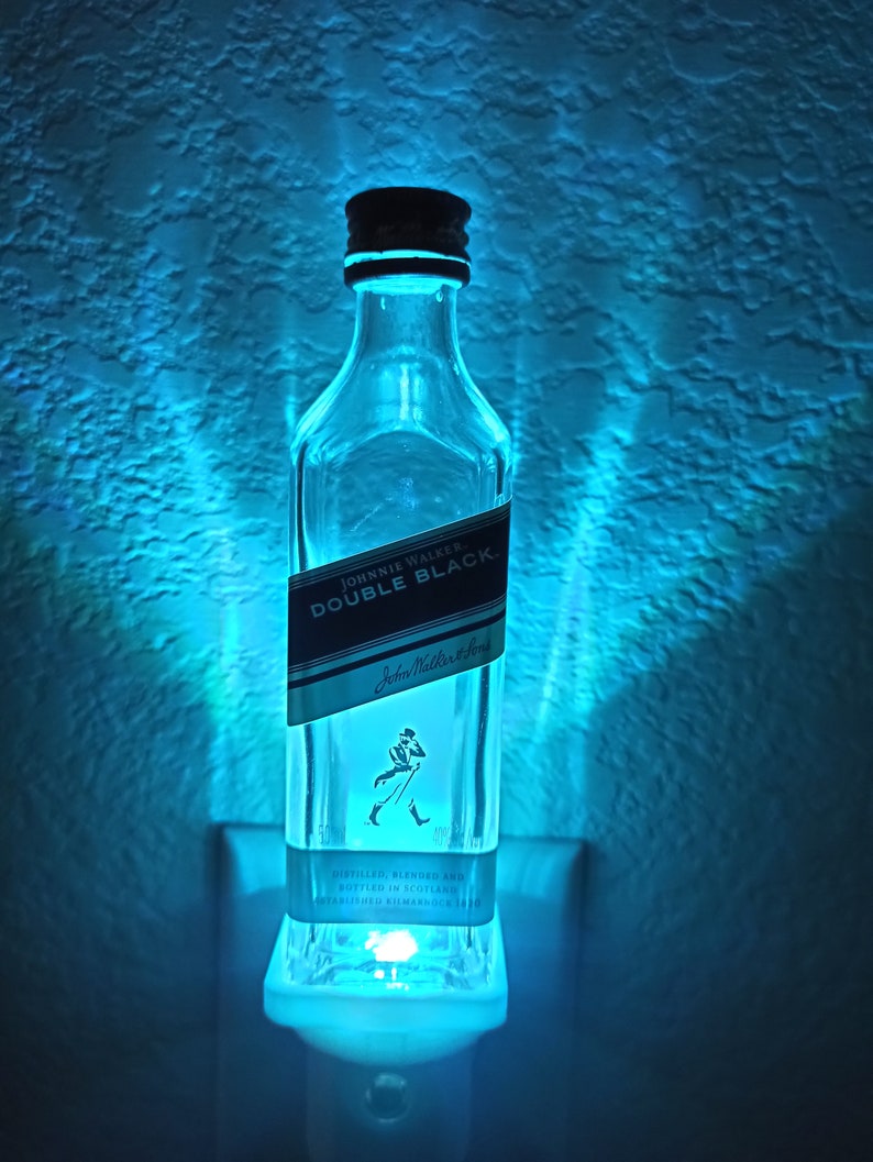 May include: A clear glass bottle night light shaped like a Johnnie Walker Double Black whisky bottle. The bottle is lit from the inside with a blue light.