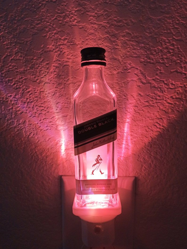 May include: A clear glass bottle with a white label that reads "JOHNNIE WALKER. DOUBLE BLACK." The bottle is lit from the inside with a pink light and is plugged into an electrical outlet.