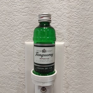 Puede incluir: Una botella de vidrio verde de ginebra seca Tanqueray London Dry Gin, con una tapa plateada, est&aacute; enchufada en una toma de corriente blanca. La botella est&aacute; etiquetada como "Tanqueray Importado" y "Ginebra seca de Londres". La etiqueta tambi&eacute;n indica "47,3% ALC. BY VOL. 194,6 PROOF".