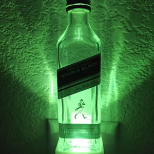 May include: A green night light made from a repurposed Johnnie Walker Double Black whisky bottle. The bottle is clear glass with a black label that reads "Johnnie Walker Double Black" and "Johnnie Walker & Sons". The label also includes the text "Distilled, Blended and Bottled in Scotland" and "Established Kilmarnock 1820".