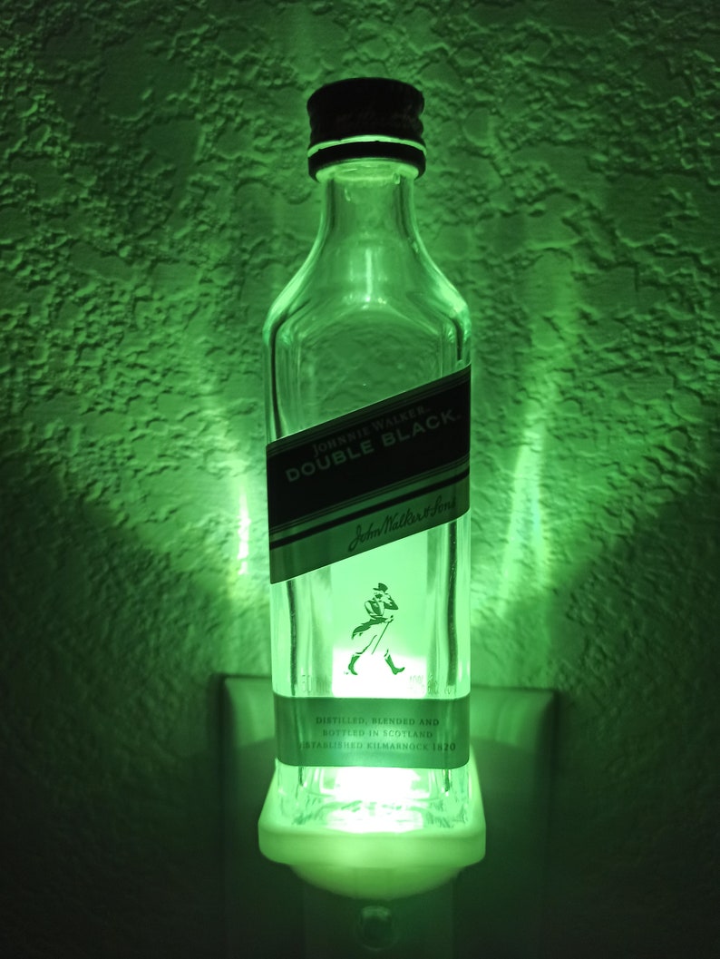 May include: A green night light made from a repurposed Johnnie Walker Double Black whisky bottle. The bottle is clear glass with a black label that reads "Johnnie Walker Double Black" and "Johnnie Walker & Sons". The label also includes the text "Distilled, Blended and Bottled in Scotland" and "Established Kilmarnock 1820".
