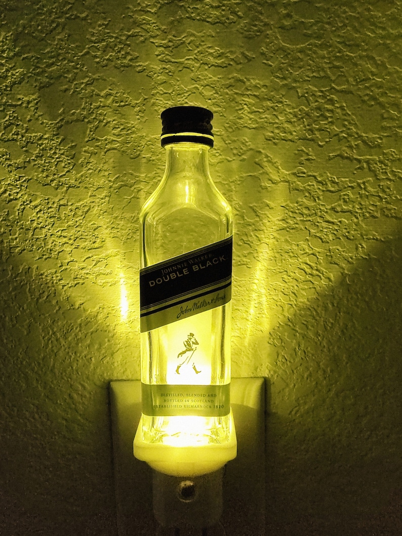 May include: A clear glass bottle night light shaped like a Johnnie Walker Double Black Scotch whisky bottle. The bottle has a black label with white text that reads "Johnnie Walker Double Black" and "Distilled, Blended and Bottled in Scotland. Established Kilmarnock 1820".