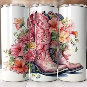 Puede incluir: Un vaso blanco con un diseño floral rosa con dos botas de vaquero rosas con detalles intrincados. Las flores son una mezcla de rosa, amarillo y blanco.