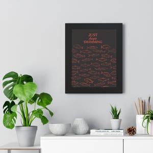 May include: Framed art print featuring a dark background with a school of fish in a reddish-orange color. The words "Just Keep Swimming" are printed in the same color at the top. The print is in a black frame.
