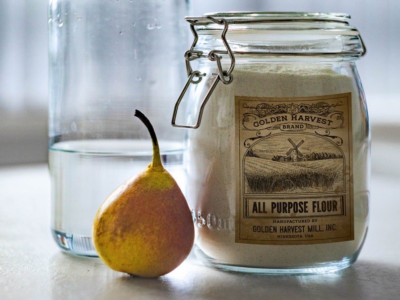 May include: A still life image featuring a glass jar of all-purpose flour with a vintage label, a yellow pear, and a glass bottle with water. The label reads "Golden Harvest Brand" and "All Purpose Flour".