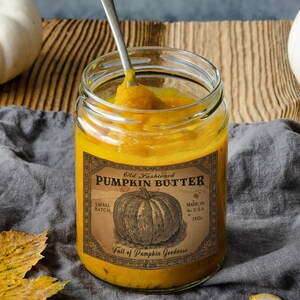 May include: A jar of pumpkin butter with a vintage label that reads "Old Fashioned Pumpkin Butter." The label features a pumpkin illustration and the text "Made in the U.S.A., 18oz." A spoon is in the jar, scooping out the orange butter. The text "Cloud Petals Co." is at the bottom.
