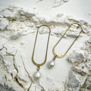 May include: A pair of gold hoop earrings with a pearl dangling from each hoop.