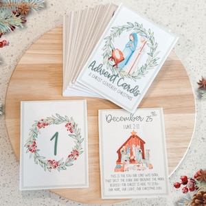 Puede incluir: Tarjetas de Adviento con ilustraciones de un pesebre y una corona con el número 1. Las tarjetas son blancas con detalles verdes y rojos. El texto "Advent Cards" y "A Christ-Centered Christmas" es visible.