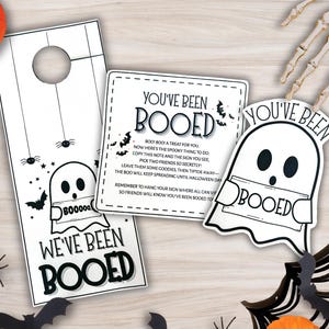Könnte beinhalten: Ein Halloween-Set mit einem Türhänger, einer Karte und einem geisterförmigen Schild, alle mit dem Text "We've Been Booed" und "You've Been Booed". Die Designs umfassen Fledermäuse, Spinnen und einen Geist. Kürbisse und dekorative Fledermäuse sind ebenfalls vorhanden.