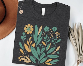 May include: Dark grey t-shirt featuring a teal and yellow floral design. The design includes leaves, flowers, and the words "diversity", "equity", and "inclusion". The shirt is made of a soft material.