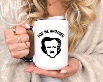 May include: White ceramic mug with a black handle and rim. The mug features a black graphic of Edgar Allan Poe's silhouette and the phrase "POE ME ANOTHER" in black lettering. A perfect gift for literature lovers.