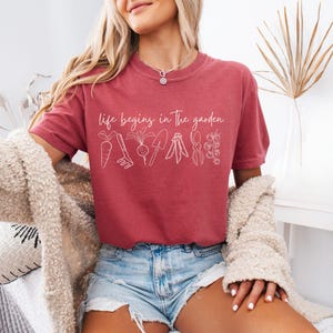 May include: A red t-shirt with the text "Life begins in the garden" and a line drawing of gardening tools and vegetables.