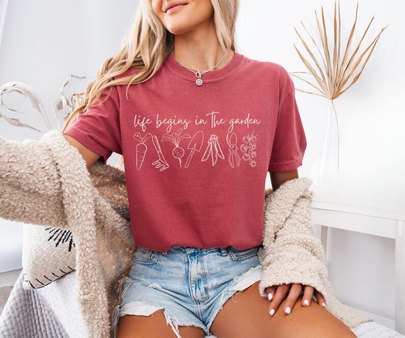 May include: A red t-shirt with the text "Life begins in the garden" and a line drawing of gardening tools and vegetables.