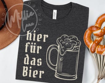 Op de afbeelding: Donkergrijs t-shirt met de Duitse zin "hier für das Bier" en een bierpul illustratie. Het shirt is gemaakt van een zacht materiaal. Een pretzel staat aan de rechterkant van het shirt.