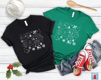 Könnte beinhalten: Zwei T-Shirts mit einem weißen Umrissdesign aus verschiedenen Back- und Weihnachtsmotiven. Das Design beinhaltet einen Mixer, einen Nudelholz, Zuckerstangen, Schneeflocken, einen Weihnachtsbaum und einen Strumpf. Ein Shirt ist schwarz und das andere grün.