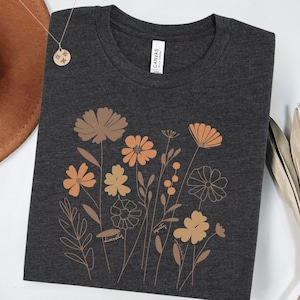 May include: A dark grey t-shirt with a floral design in shades of orange and brown. The flowers are outlined in a thin black line. The text "Beautifully" and "Perfectly" is written in a script font at the bottom of the design.
