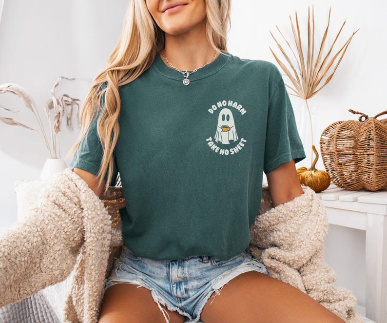 Peut inclure: T-shirt vert fonc&eacute; avec un motif de fant&ocirc;me tenant une tasse de caf&eacute; et le texte "DO NO HARM TAKE NO SHEET". Le t-shirt a une coupe d&eacute;contract&eacute;e et des manches courtes. Un v&ecirc;tement d&eacute;contract&eacute;.