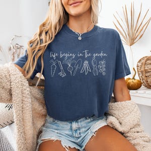 May include: A navy blue t-shirt with the text "life begins in the garden" and a white outline of gardening tools and vegetables.