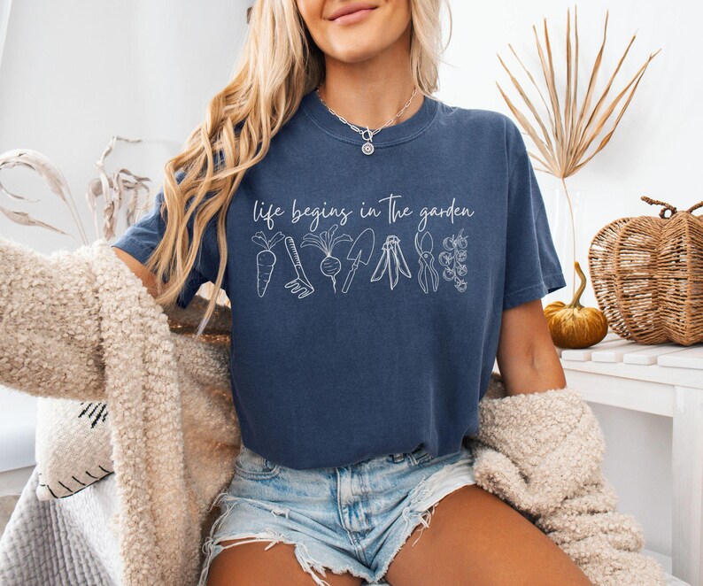 May include: A navy blue t-shirt with the text "life begins in the garden" and a white outline of gardening tools and vegetables.