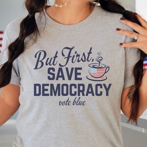 May include: Gray t-shirt with the text "But First, Save Democracy vote blue" and a coffee cup with an American flag design.