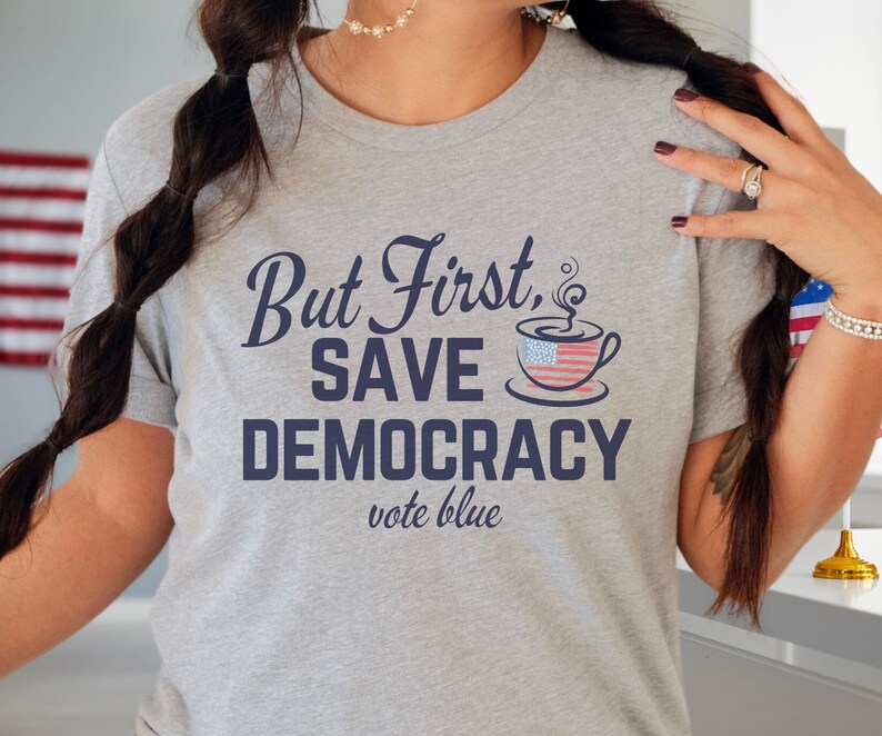 May include: Gray t-shirt with the text "But First, Save Democracy vote blue" and a coffee cup with an American flag design.