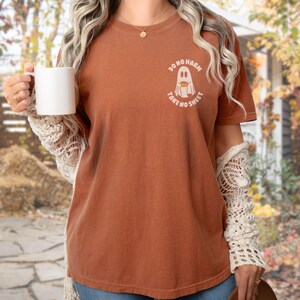 Peut inclure: Un t-shirt couleur rouille avec le texte "DO NO HARM TAKE NO SHEET" et un motif de fant&ocirc;me. Le t-shirt est &agrave; col rond et &agrave; manches courtes. La personne tient une tasse blanche et porte une manche en dentelle cr&egrave;me.